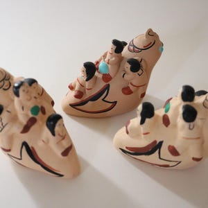 May include: Three ceramic figurines in a light tan color, each depicting a group of small figures riding on a stylized bird. The figurines have black, red, and green accents. The background is white.