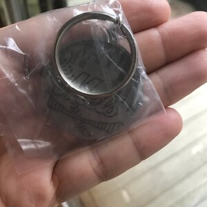 May include: A silver keychain with a circular design featuring a skull and crossbones. The keychain is packaged in a clear plastic bag.