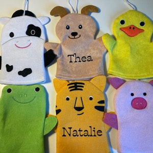 May include: Six colorful animal bath mitts with embroidered faces and names. The mitts are white cow, brown dog with "Thea" embroidered on it, yellow duck, green frog, orange tiger with "Natalie" embroidered on it, and pink pig.