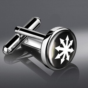 May include: A pair of silver cufflinks with a black background and a white symbol of eight arrows pointing in different directions.