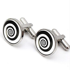 Puede incluir: Un par de gemelos de plata con un diseño en espiral blanco y negro. Los gemelos son redondos y tienen un acabado pulido.