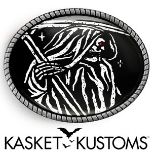 May include: A black and white belt buckle with a silver rim. The buckle features a grim reaper with a scythe and a red eye. The text "KASKET KUSTOMS" is printed below the buckle.