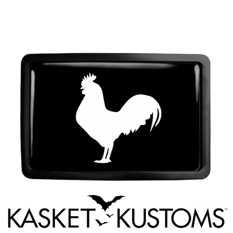 May include: Black and white rooster silhouette on a black background. The rooster is facing right and has a large comb and wattles. The image is in a rectangular frame.