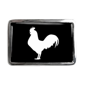 May include: A silver belt buckle with a black background and a white silhouette of a rooster.