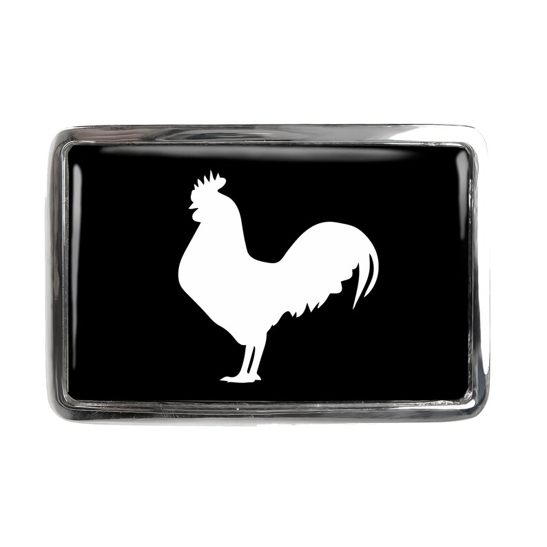 May include: A silver belt buckle with a black background and a white silhouette of a rooster.