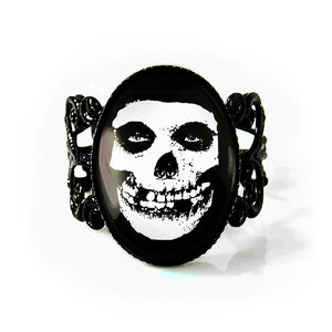 May include: Black and white Misfits skull image on a black cameo style ring. The ring is made of metal with a decorative design.