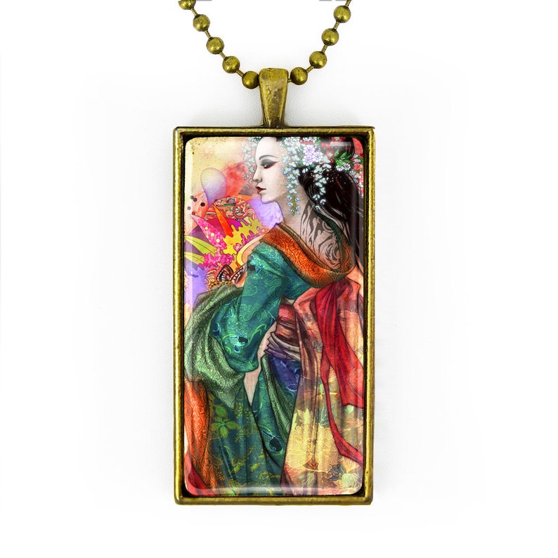 May include: A rectangular pendant necklace with a bronze-colored frame. The pendant features a colorful illustration of a woman in a traditional Japanese kimono. The woman has dark hair and is adorned with flowers. The background has a mix of colors.