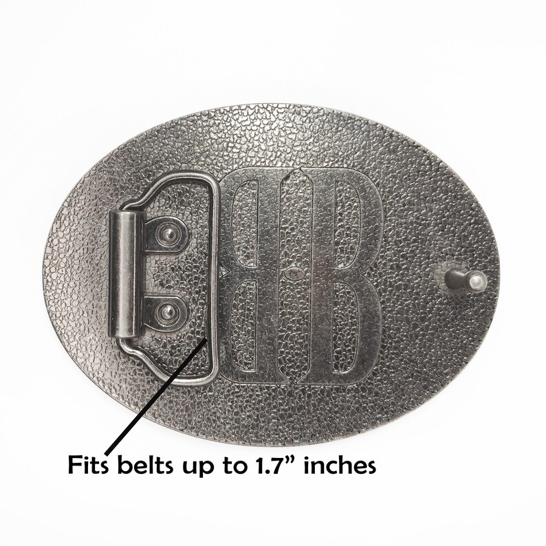 May include: Silver-toned metal belt buckle with a textured surface. The buckle features a raised design of the letter "B". It fits belts up to 1.7 inches wide.