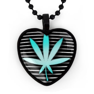 Puede incluir: Collar con colgante en forma de corazón negro con un diseño de hoja de marihuana turquesa sobre un fondo rayado en blanco y negro.