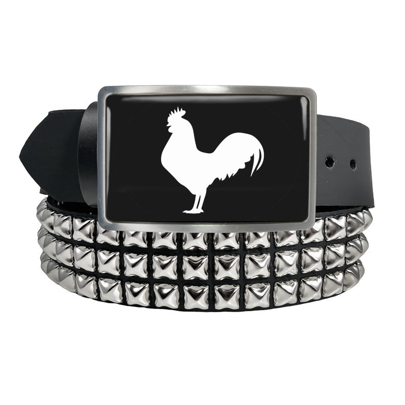 May include: A black leather belt with a silver buckle featuring a white rooster silhouette. The belt has multiple rows of silver pyramid-shaped studs.
