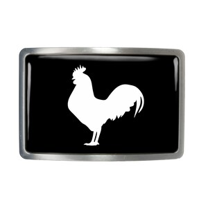 May include: A silver belt buckle with a black background and a white silhouette of a rooster.
