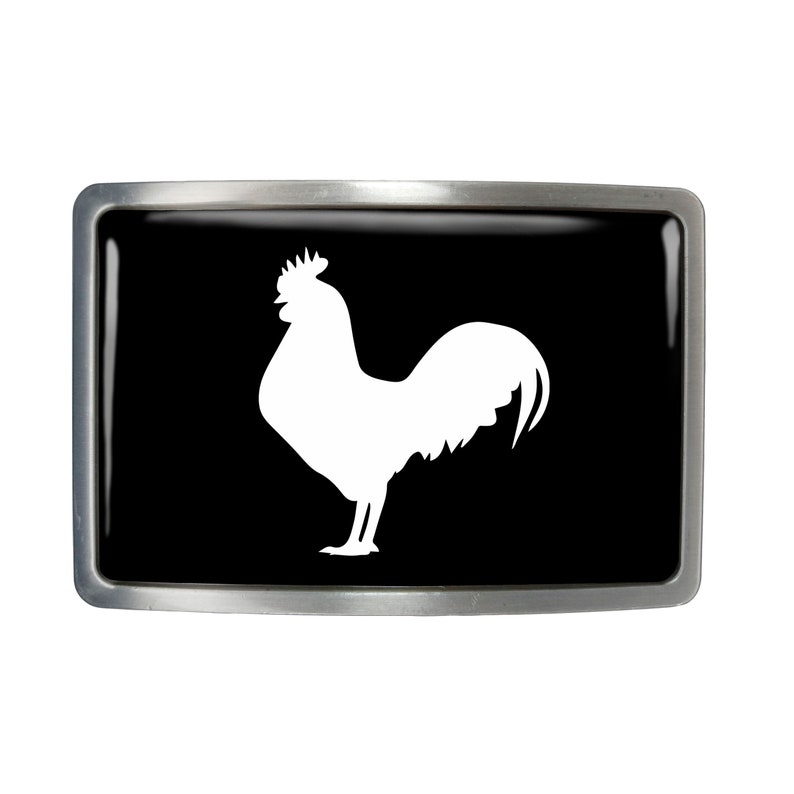 May include: A silver belt buckle with a black background and a white silhouette of a rooster.