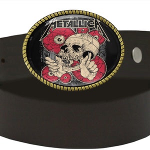 Puede incluir: Un cintur&oacute;n de cuero marr&oacute;n con una hebilla de metal que presenta una calavera con ojos rojos y la palabra "METALLICA" en letras blancas.