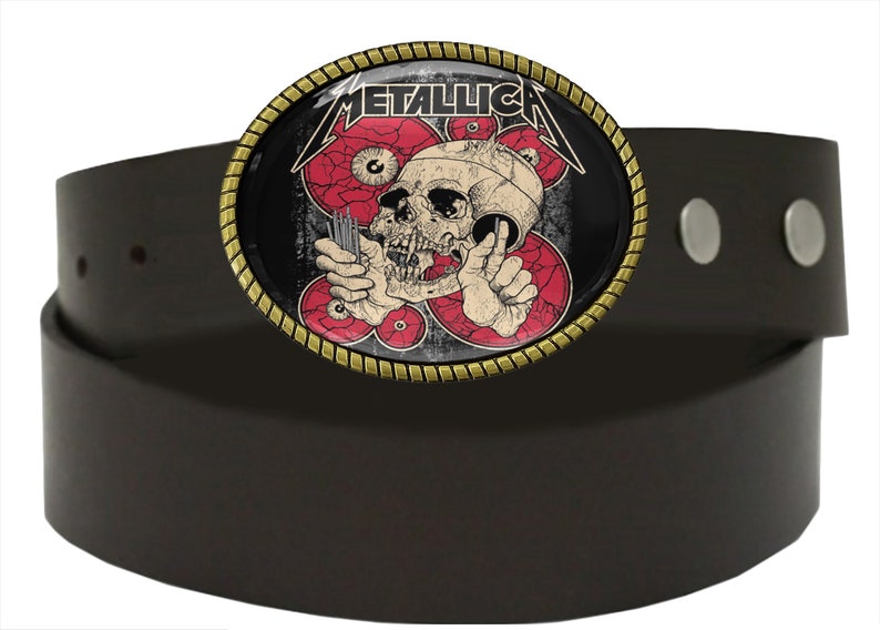 Puede incluir: Un cintur&oacute;n de cuero marr&oacute;n con una hebilla de metal que presenta una calavera con ojos rojos y la palabra "METALLICA" en letras blancas.