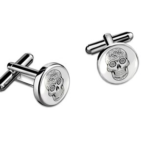 May include: A pair of silver cufflinks with a round, white enamel design featuring a black and white sugar skull.