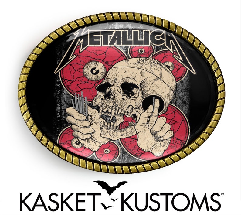 Puede incluir: Una hebilla de cintur&oacute;n ovalada negra y dorada con un dise&ntilde;o de calavera y huesos cruzados. La calavera sostiene un juego de agujas y est&aacute; rodeada de ojos rojos. El texto "METALLICA" est&aacute; impreso en blanco en la hebilla.