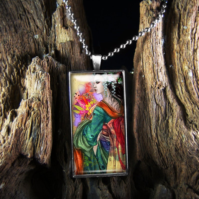 May include: A rectangular pendant necklace with a silver chain. The pendant features a colorful illustration of a woman in a green and red kimono with a floral headdress. The background is a mix of yellow, pink, and purple.