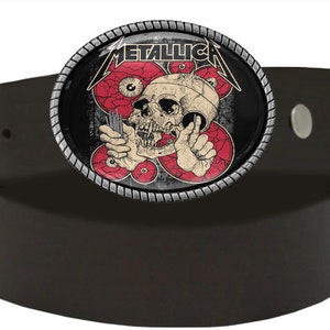Puede incluir: Un cintur&oacute;n de cuero negro con una hebilla de metal plateado que presenta una calavera con ojos rojos y la palabra "METALLICA" en letras blancas.