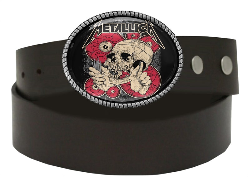 Puede incluir: Un cintur&oacute;n de cuero negro con una hebilla de metal plateado que presenta una calavera con ojos rojos y la palabra "METALLICA" en letras blancas.