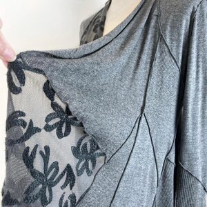 以下が含まれることがあります： グレーのロングスリーブトップ。カウルネックと、サイドにブラックのフローラルレースパネルが付いている。