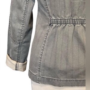 May include: A gray striped jacket with a cinched waist and long sleeves. The jacket has a white lining on the inside of the sleeves.
