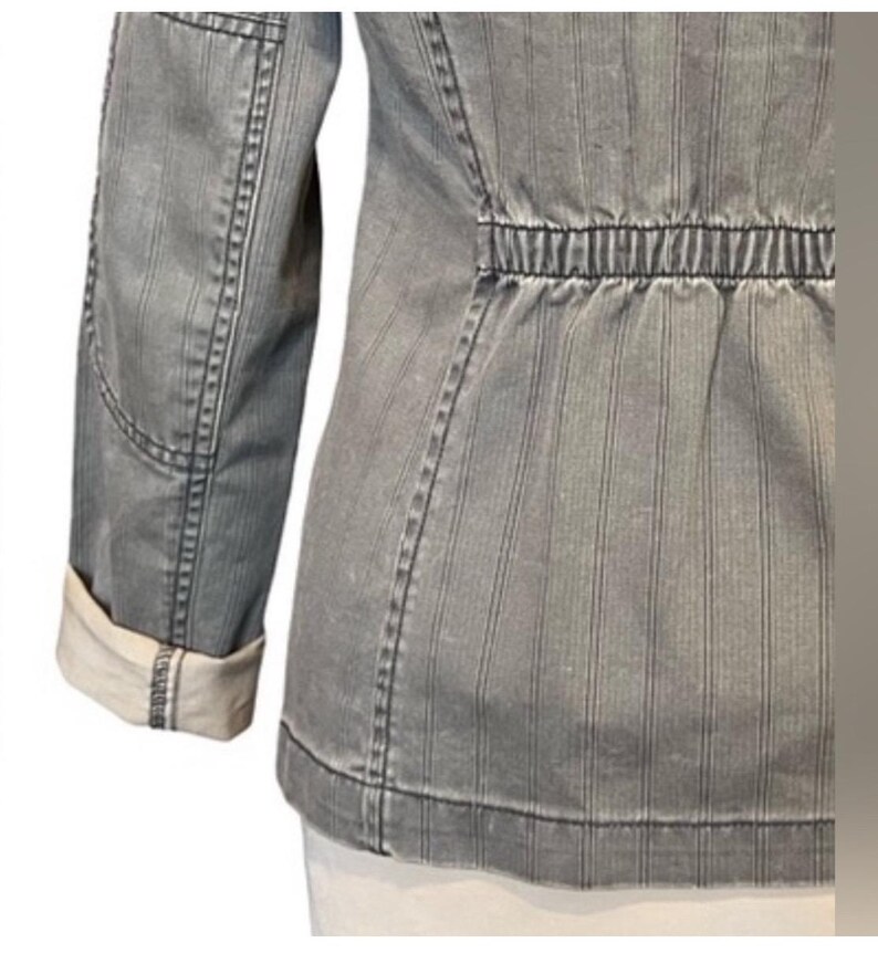 May include: A gray striped jacket with a cinched waist and long sleeves. The jacket has a white lining on the inside of the sleeves.