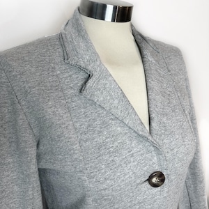 Op de afbeelding: Een grijze blazer met een enkele knoopsluiting. De blazer is gemaakt van een zachte, gestructureerde stof.