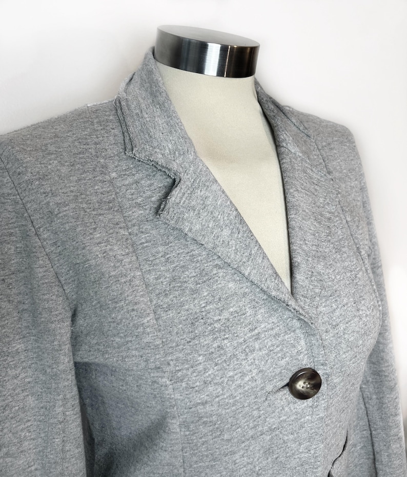 Op de afbeelding: Een grijze blazer met een enkele knoopsluiting. De blazer is gemaakt van een zachte, gestructureerde stof.