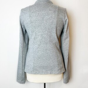 Op de afbeelding: Een grijze blazer met lange mouwen en een kraag. De blazer is gemaakt van een zachte, rekbare stof.