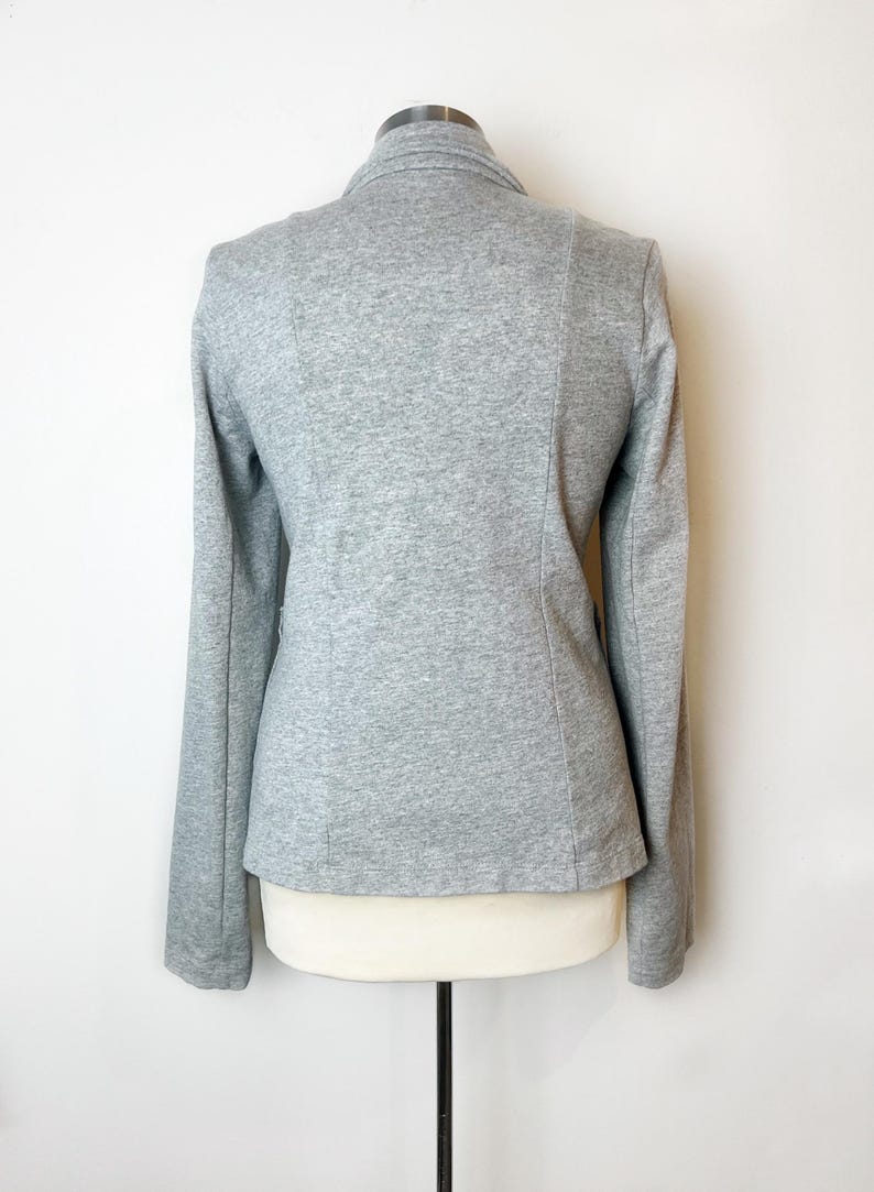 Op de afbeelding: Een grijze blazer met lange mouwen en een kraag. De blazer is gemaakt van een zachte, rekbare stof.