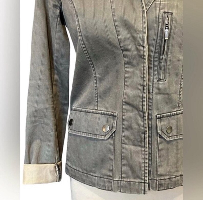May include: A gray striped denim jacket with a zipper closure and two flap pockets. The jacket has a slightly fitted silhouette and a collar.