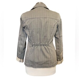 May include: A gray striped denim jacket with a cinched waist and long sleeves. The jacket has a button closure and a collar.