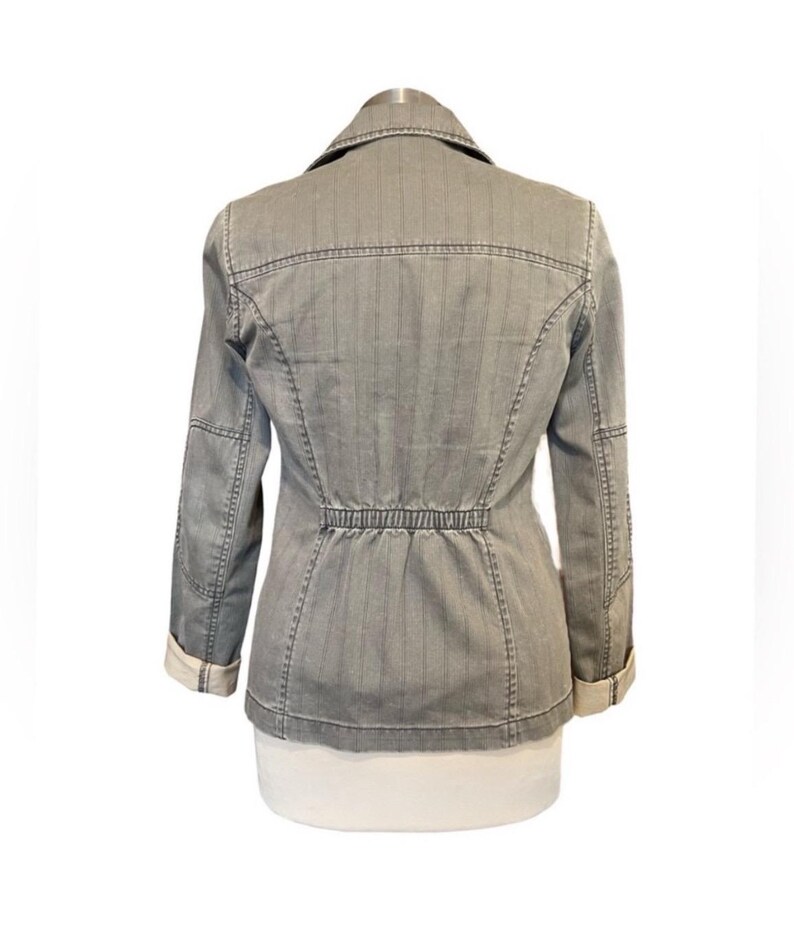 May include: A gray striped denim jacket with a cinched waist and long sleeves. The jacket has a button closure and a collar.