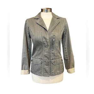 May include: A gray denim jacket with a zipper closure and two flap pockets. The jacket has a collar and long sleeves.