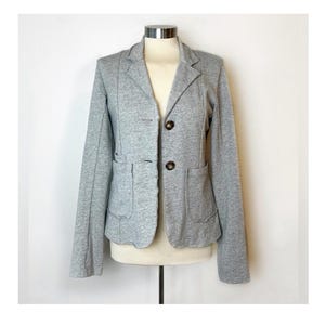 Op de afbeelding: Een grijze blazer met twee zakken en drie knopen. De blazer heeft een licht getailleerde pasvorm.