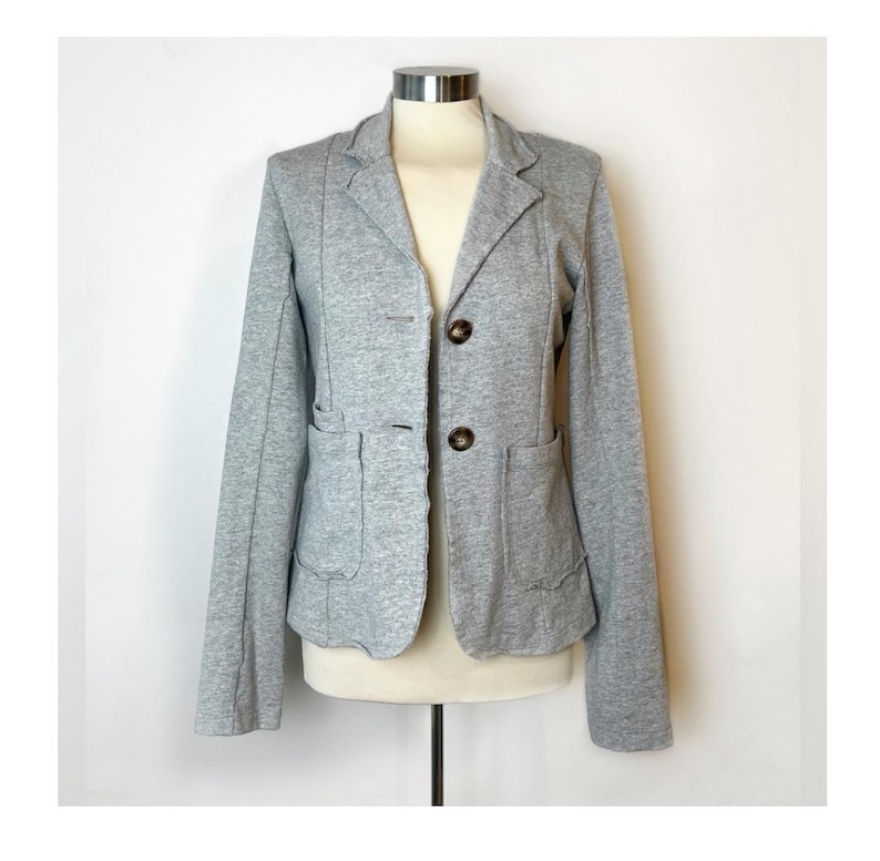 Op de afbeelding: Een grijze blazer met twee zakken en drie knopen. De blazer heeft een licht getailleerde pasvorm.
