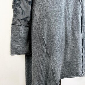 以下が含まれることがあります： 袖に黒いレースのディテールが付いたグレーの長袖チュニック。チュニックはわずかに非対称なヘムラインです。