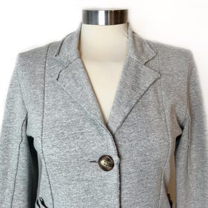 Op de afbeelding: Een grijze blazer met een enkele knoopsluiting. De blazer heeft een reverskraag en lange mouwen.