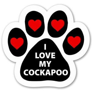 May include: A paw-shaped sticker with a white border, featuring a black paw print design. Each pad has a red heart. The text "I LOVE MY COCKAPOO" is in white letters on the bottom of the paw print.