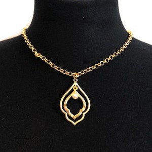 Könnte beinhalten: Eine goldene Kettenkette mit einem Anhänger in Form eines doppelten Tränen-Designs mit einer Perle in der Mitte.
