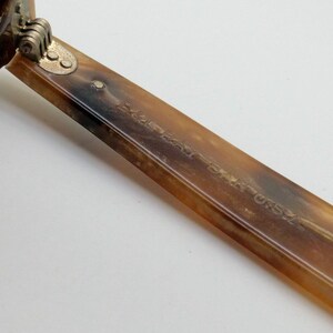May include: Close-up of a pair of sunglasses with a tortoiseshell pattern. The arm of the glasses is visible, with the text "MADE IN USA" etched into the surface. The hinge is a gold color.