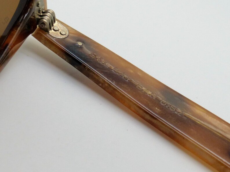 May include: Close-up of a pair of sunglasses with a tortoiseshell pattern. The arm of the glasses is visible, with the text "MADE IN USA" etched into the surface. The hinge is a gold color.