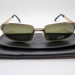 Puede incluir: Gafas de sol con montura dorada y lentes verdes sobre un estuche de cuero negro. Las gafas tienen forma rectangular y patillas negras. El estuche tiene un dise&ntilde;o en relieve y el logotipo de Versace.