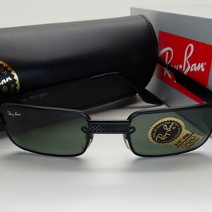Puede incluir: Gafas de sol Ray-Ban negras con lentes verdes y montura negra. Las gafas se muestran con un estuche negro y una caja con el logotipo de Ray-Ban. Las lentes tienen una pegatina que dice "100% UV protection".