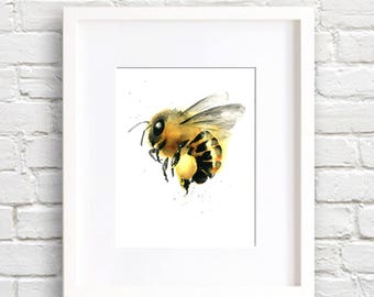 May include: A framed watercolor print of a bee. The bee is depicted in shades of yellow, black, and brown, with delicate wings and fine details. The artwork is set against a white background and framed in a white border, suitable for home decor.