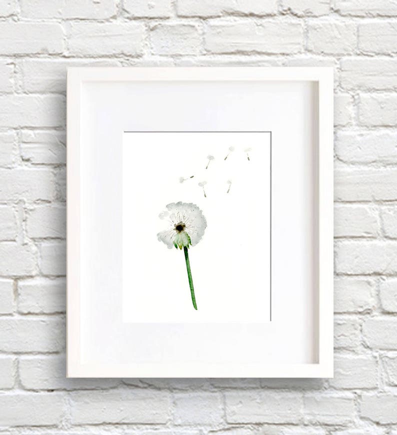 May include: A framed print featuring a watercolor painting of a dandelion. The white dandelion head is partially blown, with several seeds floating away. The stem is green, and the artwork is set against a white background.