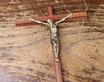 May include: A wooden crucifix with a bronze figure of Jesus Christ. The cross is made of dark brown wood, and the figure is detailed with outstretched arms. The crucifix is displayed on a wooden surface.