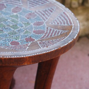 May include: A wooden stool with three legs and a round top. The top is decorated with a colourful geometric pattern made of small beads.