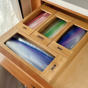 May include: A bamboo drawer organizer with five compartments for storing plastic bags. The compartments are labeled "quart", "sandwich", "snack", "gallon", and "quart".