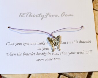 May include: A white card with the text "12 Thirty Five.Com" and instructions for making a wish. A silver butterfly charm is attached to a purple string bracelet.